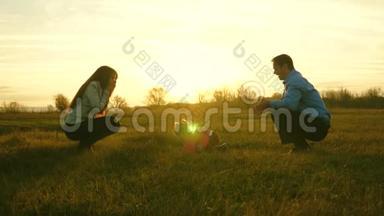 爸爸妈妈和他们的女儿在日落时在草地上玩。 家庭幸福的概念。 宝宝从爸爸到妈妈都去草坪